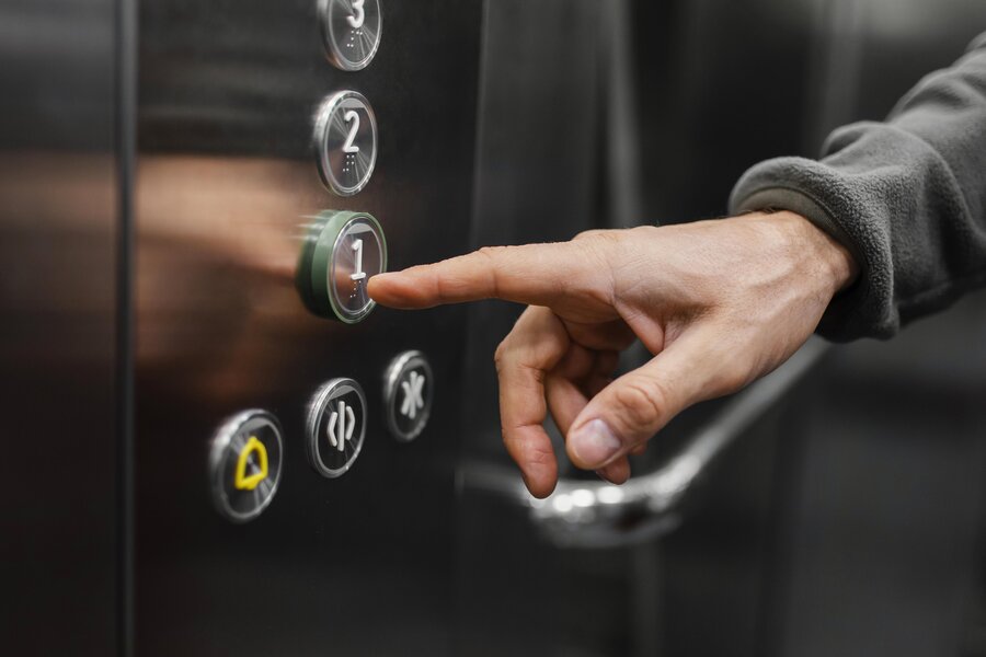Ein Finger der den Knopf von einem Fahrstuhl betätigt