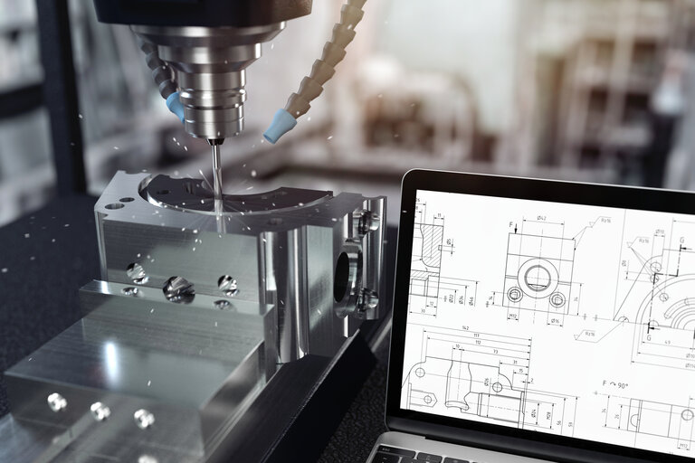 CNC-Fräse in Bearbeitung neben CAD-Zeichnungen auf Laptop – repräsentativ für beschichtete Fräswerkzeuge, Stempel, Matrizen sowie Werkzeuge für Aluminiumdruckguss und Kunststoffverarbeitung im Werkzeug- und Formenbau
