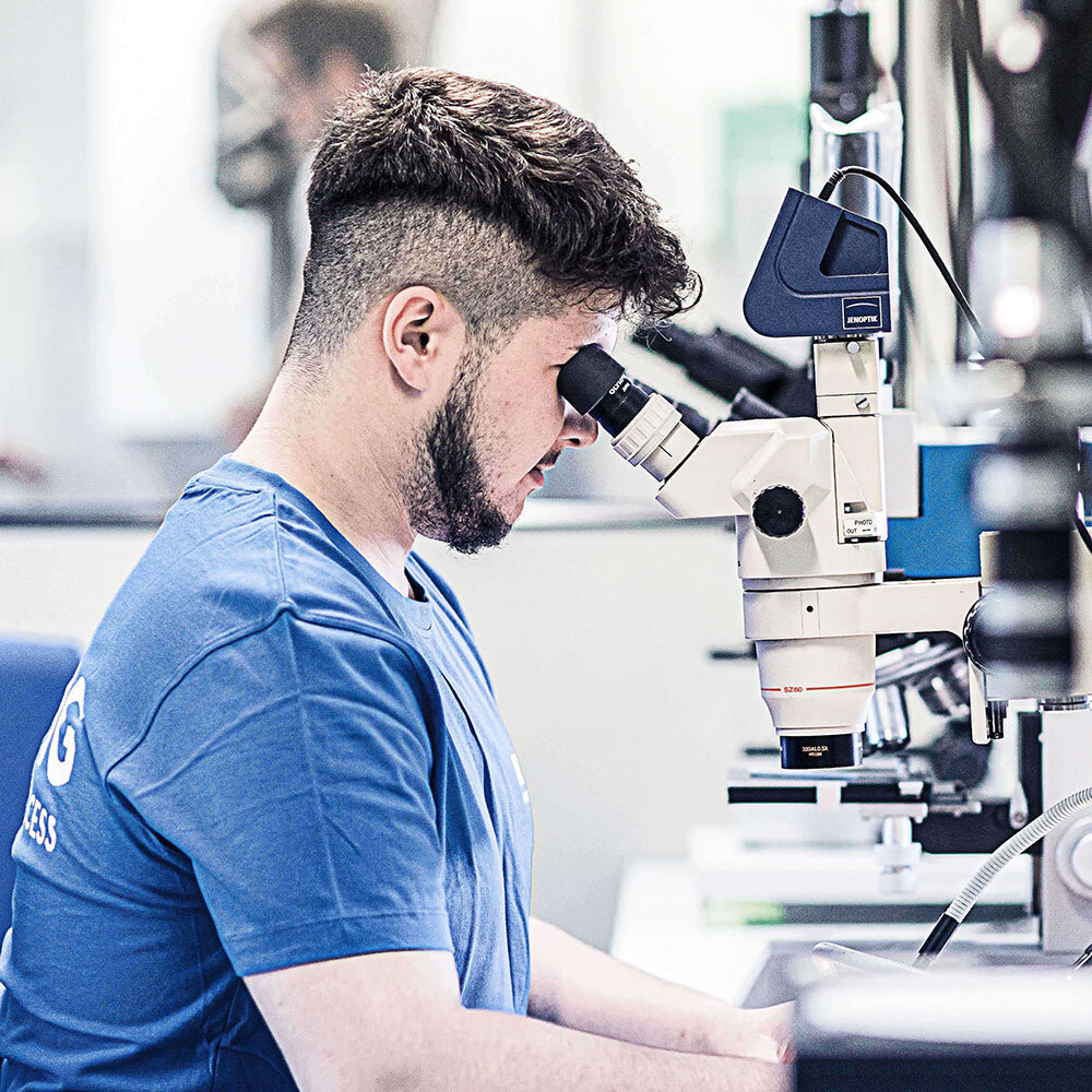 junger Mann in einem blauen RÜBIG Shirt sitzt vor einem Mikroskop