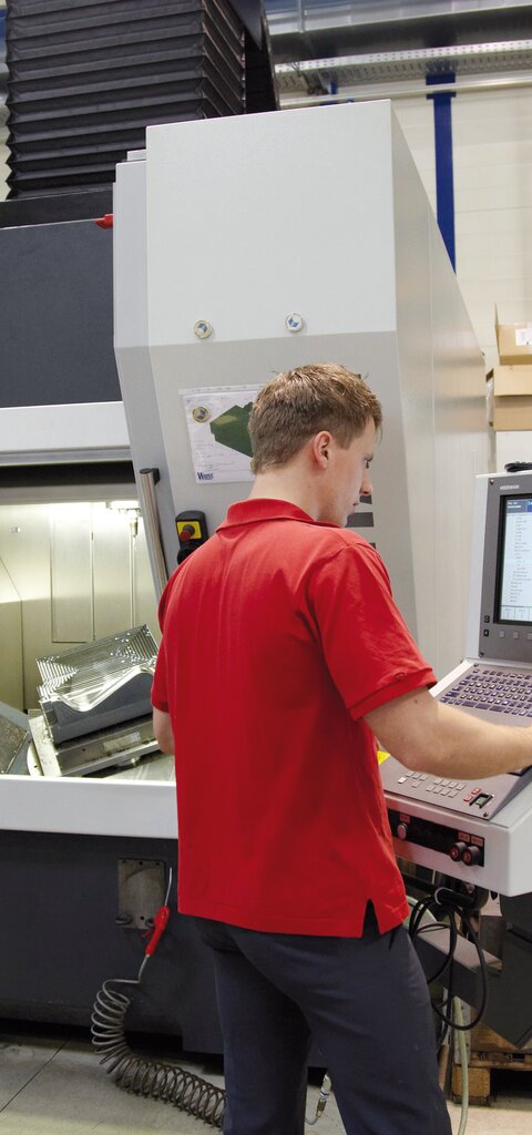 Ein junger RÜBIG-Mitarbeiter mit rotem Shirt bedient eine Pressmaschine.