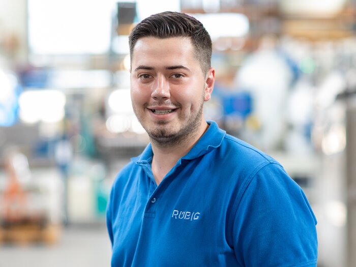 RÜBIG Mitarbeiter lächelnd im blauen Polohemd in einer Produktionshalle