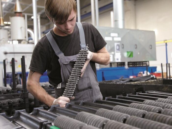 blonder RÜBIG Mitarbeiter in einem grauen Overall und schwarzen T-Shirt beim Betrachten von Bauteilen in einer Fabrikhalle