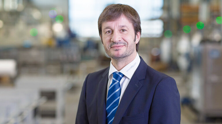 RÜBIG-Mitarbeiter im Anzug vor unscharfem industriellen Hintergrund