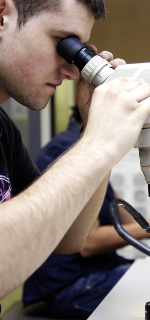 Ein RÜBIG Mitarbeiter vor einem Mikroskop beim Untersuchen von Bauteilen 